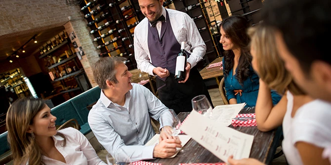 Waiter holding bottle of wine for a table of customers.